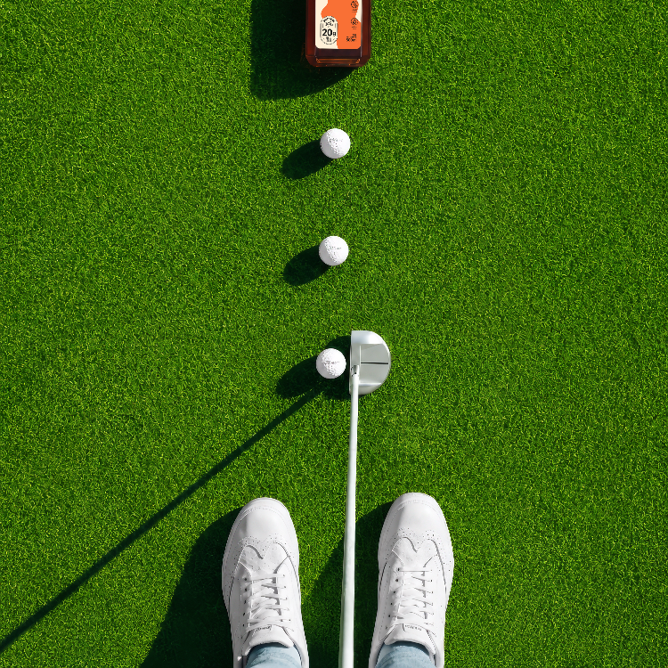 Golf putting setup with golf ball,and Heyami Protein tea on a green grass surface